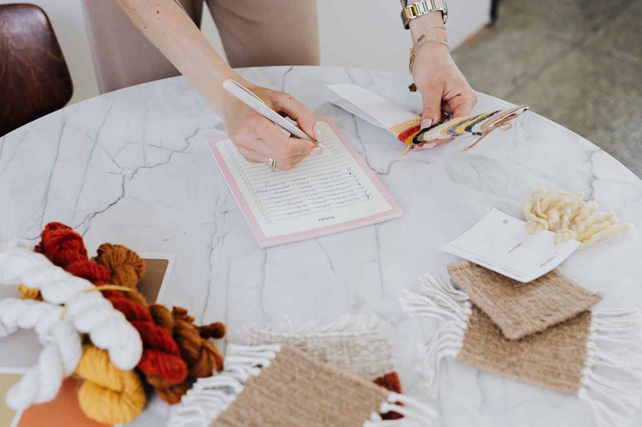 Close-up of hands working with wool and swatch samples on a marble desk.