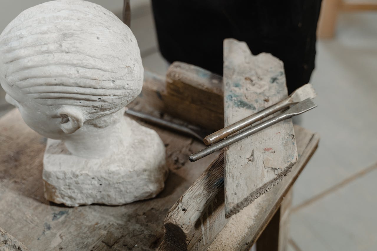 A marble sculpture head on a rustic wooden table with chiseling tools in an artist's studio.